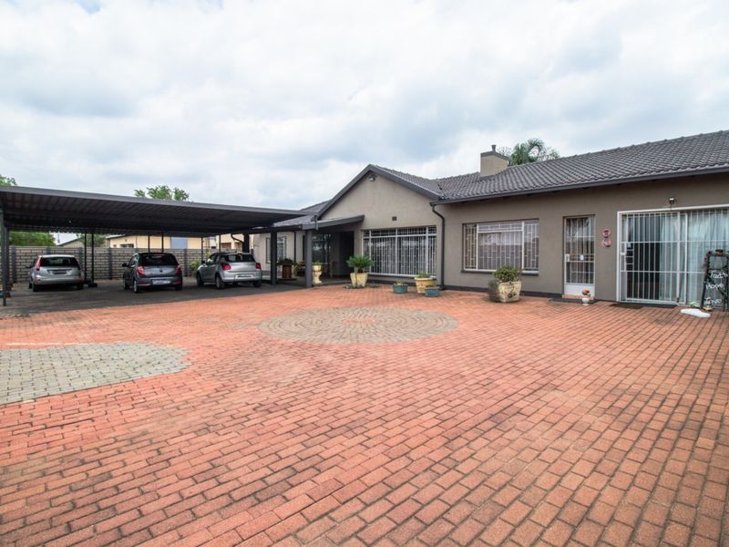 Spacious front exterior featuring a large paved driveway, a covered carport, and secure access points to the main residence.