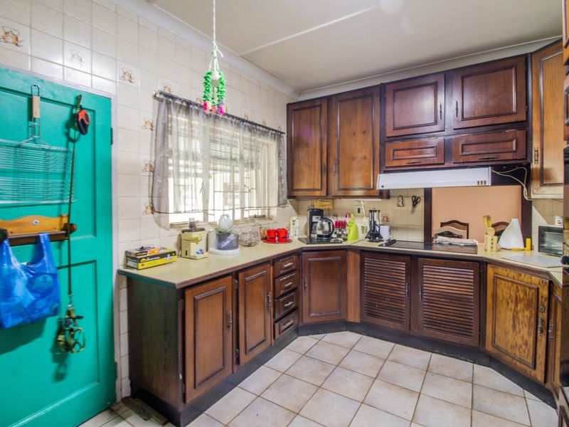 A dated kitchen featuring traditional wooden cabinetry, ceramic wall and floor tiles, and built-in cooking appliances, offering potential for a modern renovation.