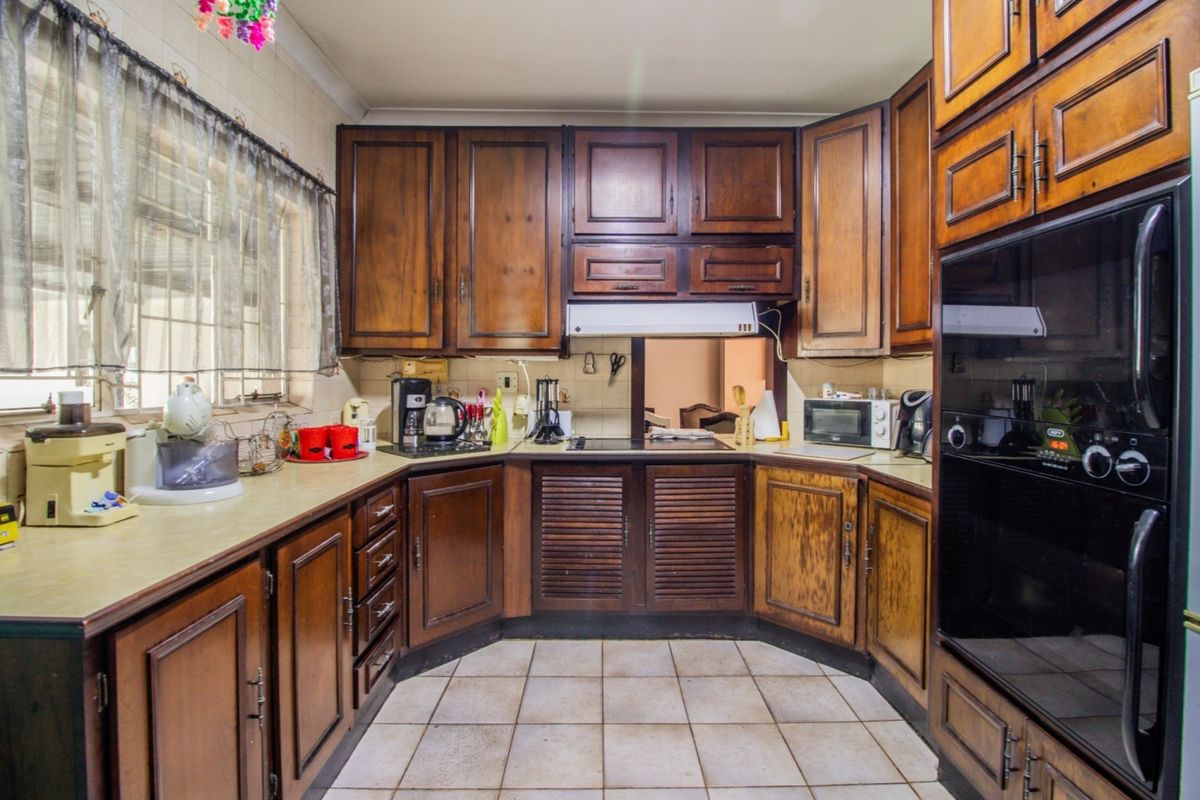A traditional kitchen featuring dark wood cabinetry, laminate countertops, built-in oven, and ceramic tile flooring, offering a functional layout with classic finishes.