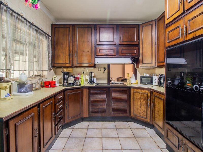 A traditional kitchen featuring dark wood cabinetry, laminate countertops, built-in oven, and ceramic tile flooring, offering a functional layout with classic finishes.