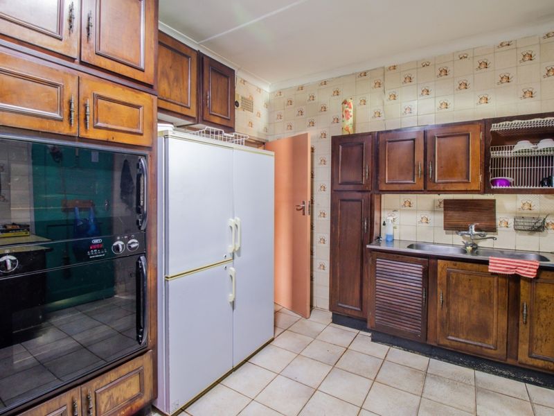 A dated kitchen featuring traditional wooden cabinetry, a stainless steel sink, built-in oven, and patterned tiled backsplash with tiled flooring.