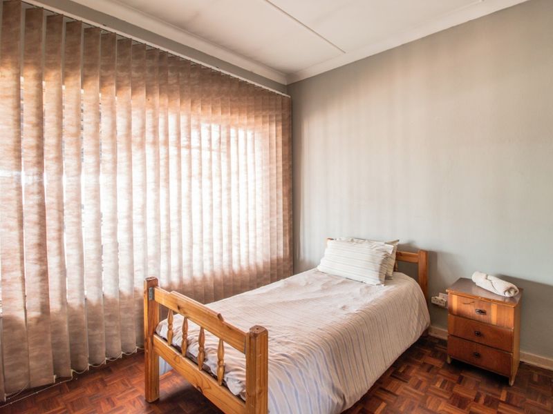 A bedroom featuring parquet flooring and vertical blinds, providing a functional space with neutral wall finishes.