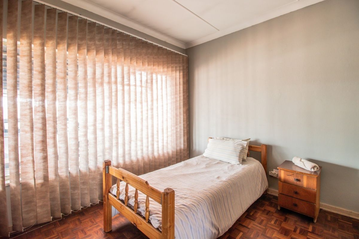 A bedroom featuring parquet flooring and vertical blinds, providing a functional space with neutral wall finishes.