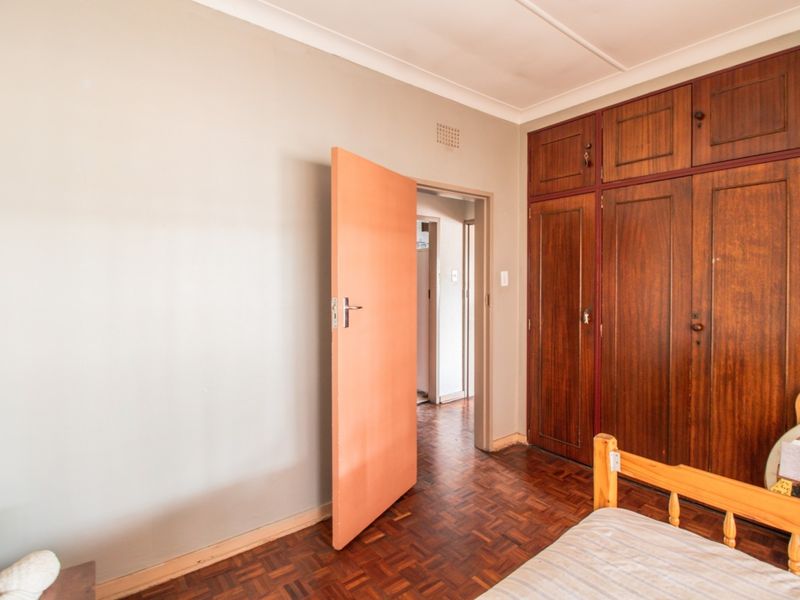 Bedroom featuring classic parquet flooring and extensive built-in wooden cabinetry, offering ample storage space within a neutral-toned room.