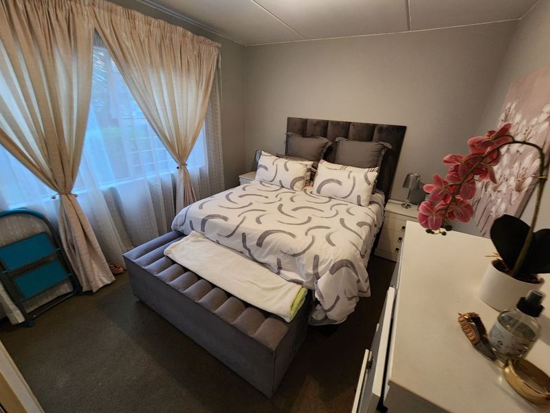 A functional bedroom featuring carpeted flooring and large windows with installed curtain tracks, providing natural light and a neutral base for interior design.
