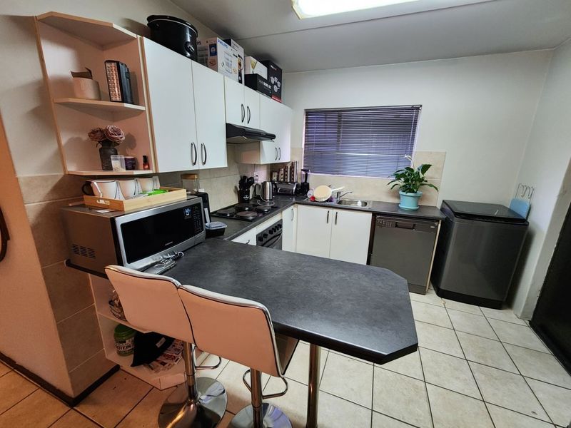Compact kitchen featuring white cabinetry, dark laminate countertops, tiled flooring, and integrated appliances, offering a functional layout for daily meal preparation.