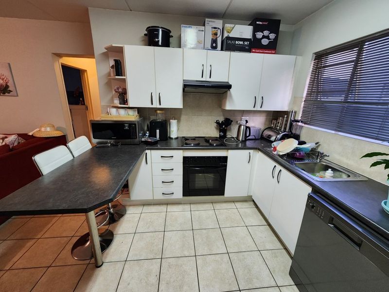 A functional kitchen featuring white cabinetry, dark laminate countertops, an integrated oven and hob, and tiled flooring with an attached breakfast bar.
