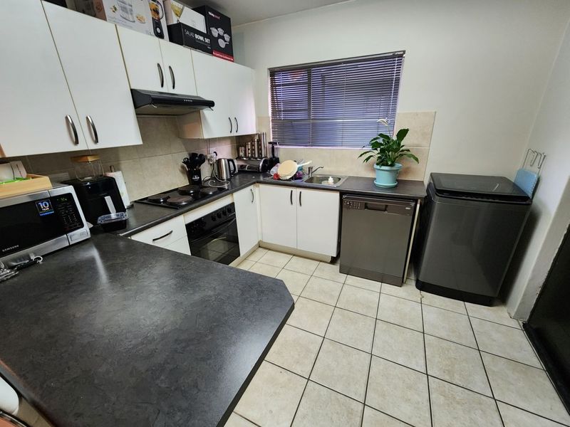 Functional kitchen featuring white cabinetry, dark laminate countertops, tiled backsplash, and integrated appliances including an oven and hob.