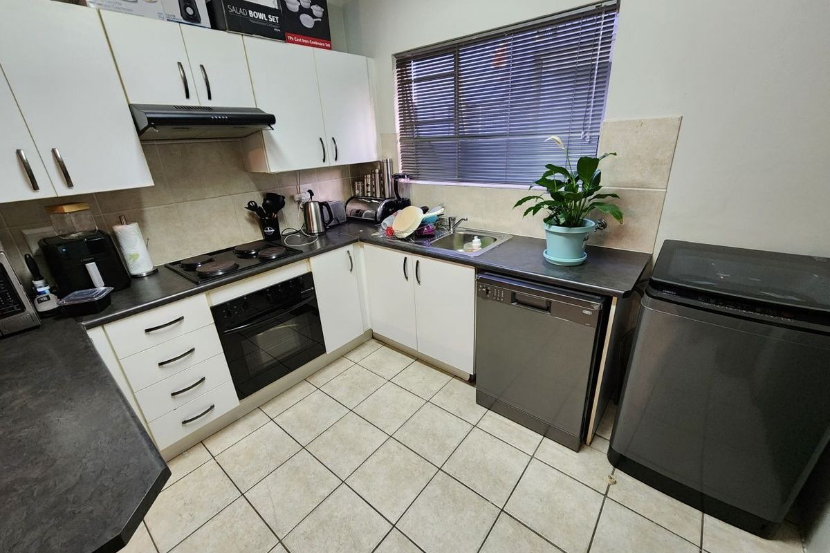 A functional kitchen featuring white cabinetry, dark laminate countertops, tiled flooring, a built-in oven with hob, and an integrated sink area.