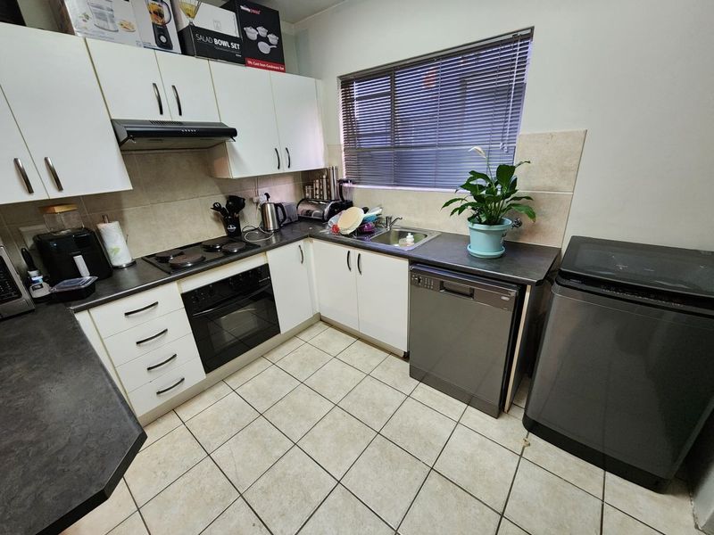 A functional kitchen featuring white cabinetry, dark laminate countertops, tiled flooring, a built-in oven with hob, and an integrated sink area.