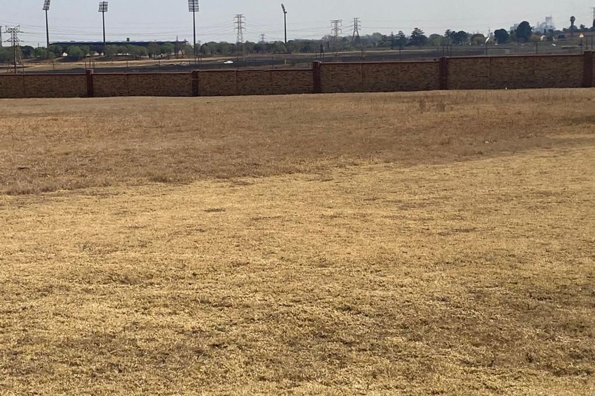 A view of a vacant residential plot featuring dry grass and a perimeter brick wall boundary.