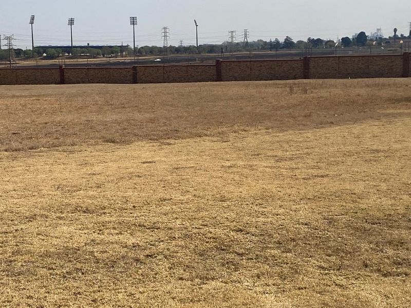 A view of a vacant residential plot featuring dry grass and a perimeter brick wall boundary.