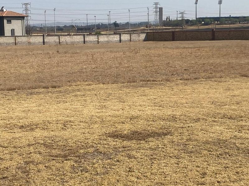 A view of a vacant residential plot featuring a perimeter brick wall and dry grass, suitable for future development.
