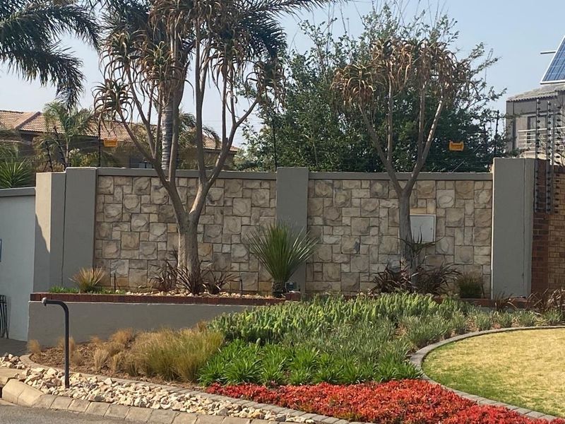 A well-maintained front boundary wall featuring stone cladding, electric fencing, and a neatly landscaped garden area.