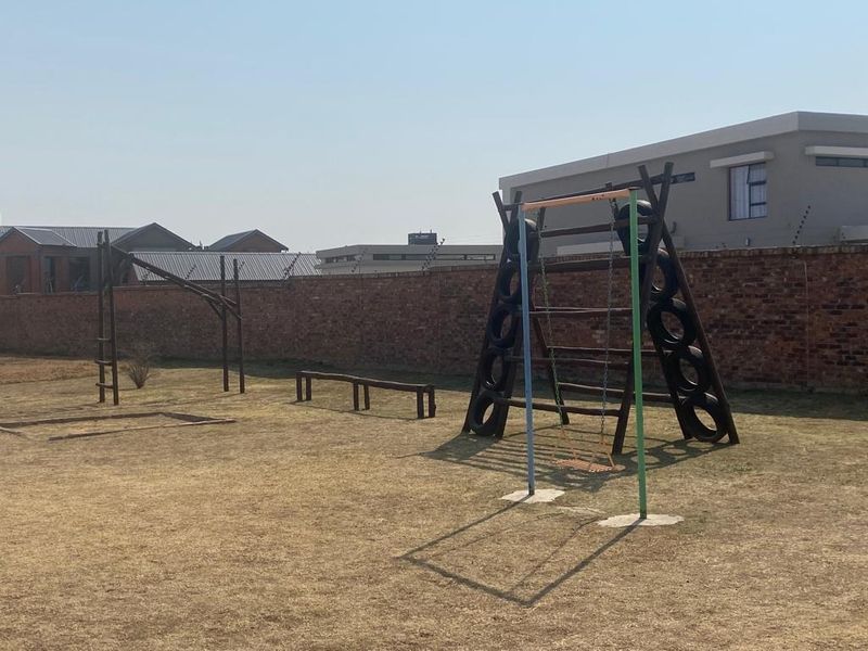 A spacious residential garden featuring a brick boundary wall with electric fencing and existing playground equipment on a dry lawn.
