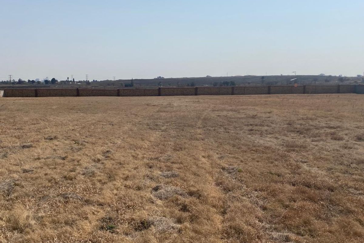 A wide, vacant residential plot featuring dry grass and a perimeter brick boundary wall.