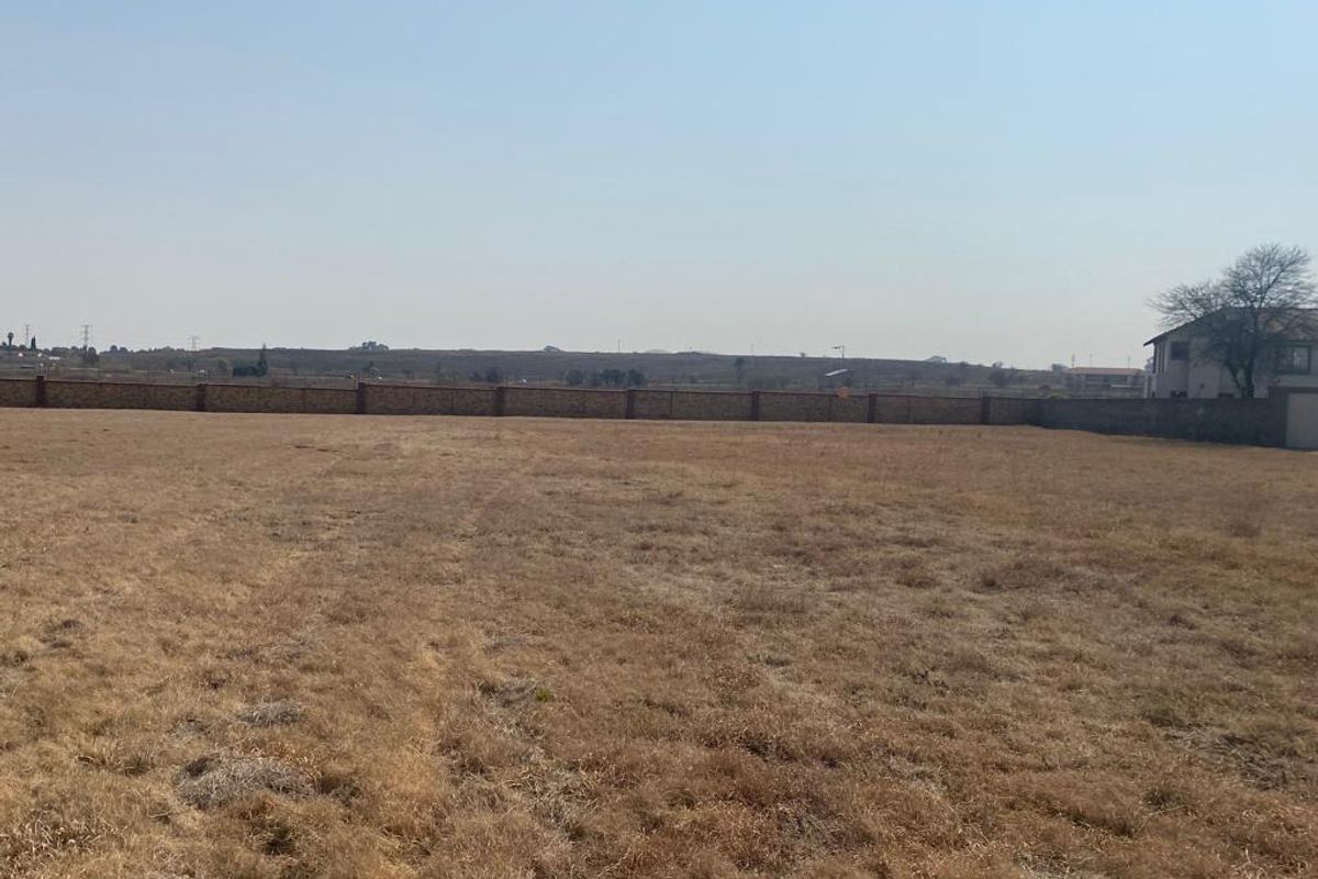 A vacant residential plot featuring dry grass and a perimeter boundary wall, offering a clear view of the surrounding landscape.