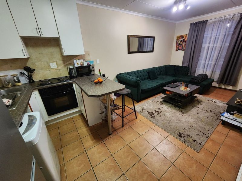 Open-plan living area featuring a compact kitchen with built-in cabinetry, electric stove, and oven, seamlessly flowing into the lounge space with tiled flooring throughout.
