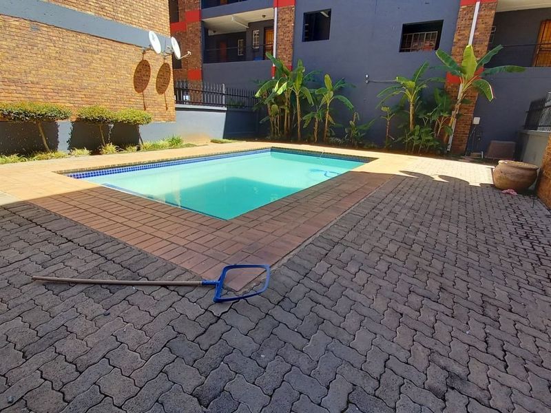 A communal swimming pool area featuring brick paving and face brick boundary walls within an apartment complex setting.