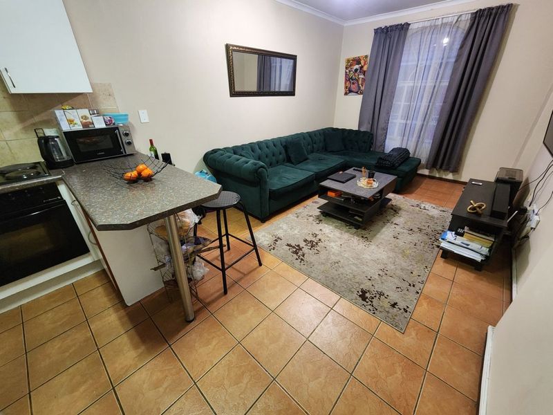 Open-plan living area featuring a compact kitchen with built-in oven, hob, and breakfast counter, seamlessly flowing into the lounge space with tiled flooring throughout.