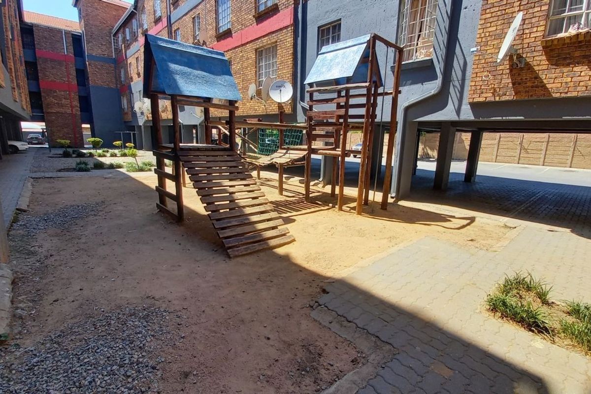 Communal outdoor area featuring a playground structure situated between apartment blocks with brick facades and paved walkways.