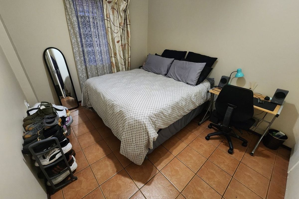 A functional bedroom featuring tiled flooring and window treatments, offering a practical space for rest and study.