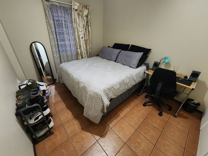 A functional bedroom featuring tiled flooring and window treatments, offering a practical space for rest and study.