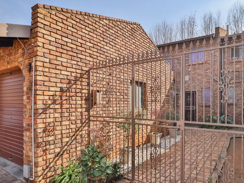 Front exterior view of a townhouse featuring a face brick facade, a secure wrought iron gate, and a roller shutter garage door.