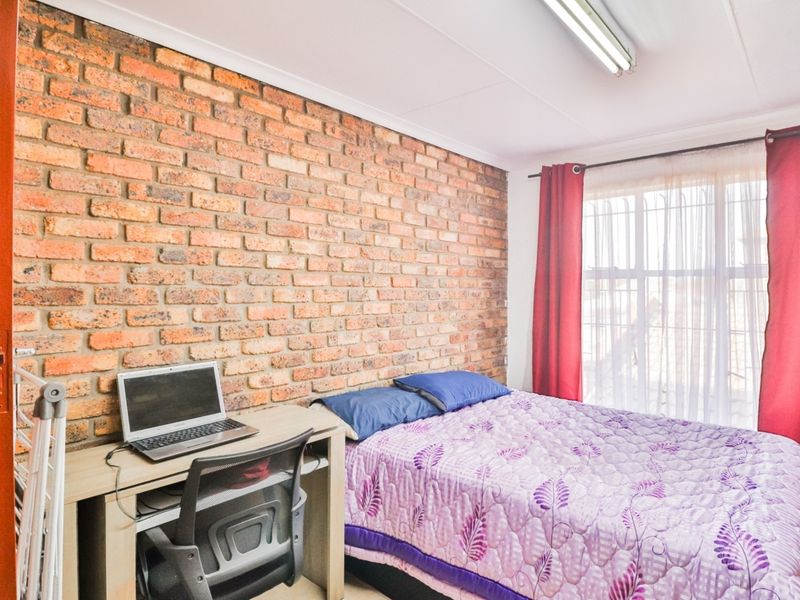 A bedroom featuring an exposed brick feature wall, a window with security bars, and a functional layout.