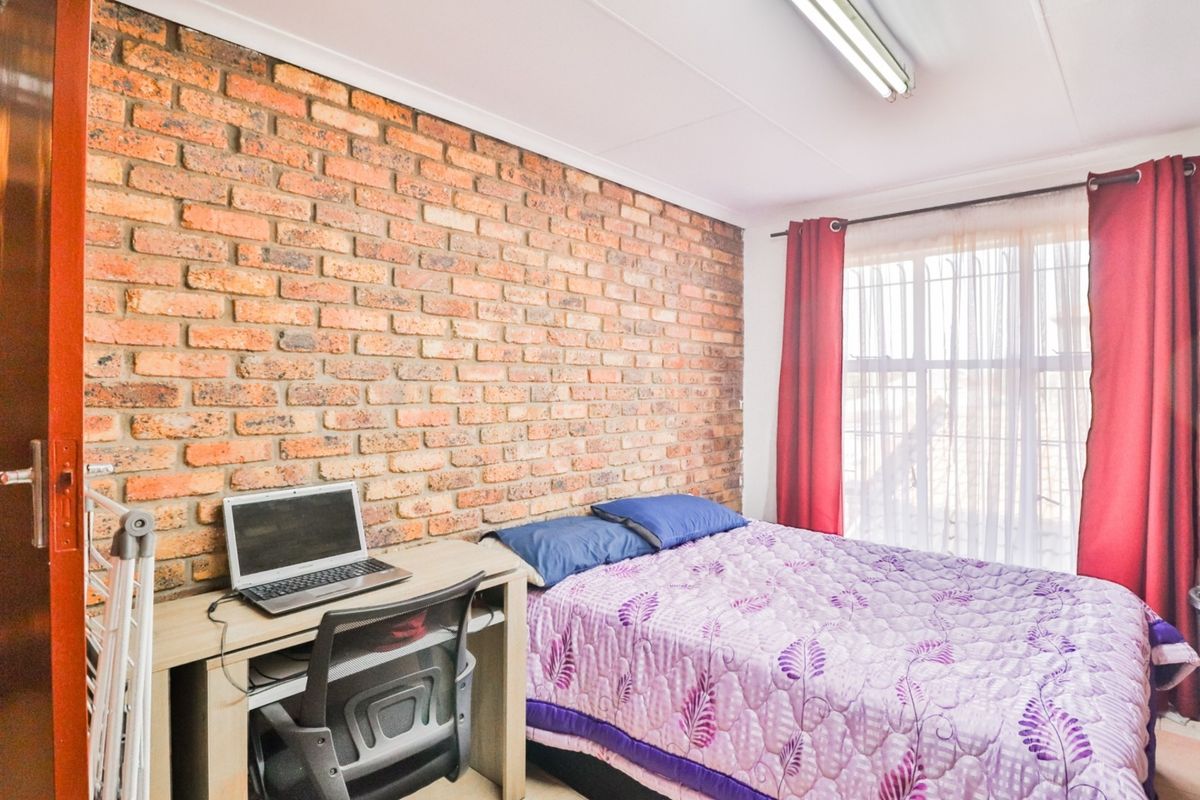 A bedroom featuring an exposed brick feature wall, a window with security bars, and a functional layout.