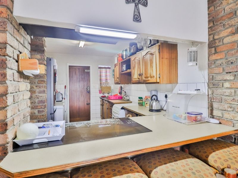 A functional kitchen featuring exposed brick walls, wooden cabinetry, and a breakfast bar, offering a rustic aesthetic with potential for modern updates.