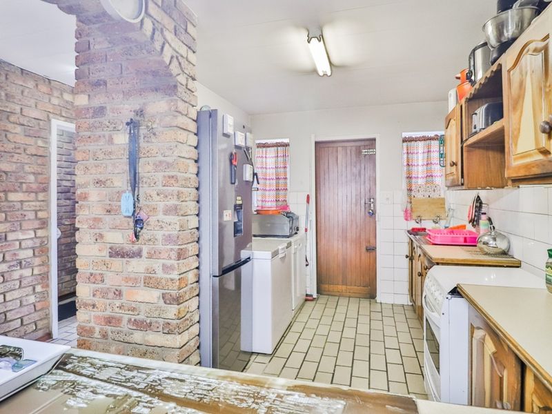 A dated kitchen featuring exposed brickwork, wooden cabinetry, tiled flooring, and a freestanding stove, offering potential for a modern renovation.