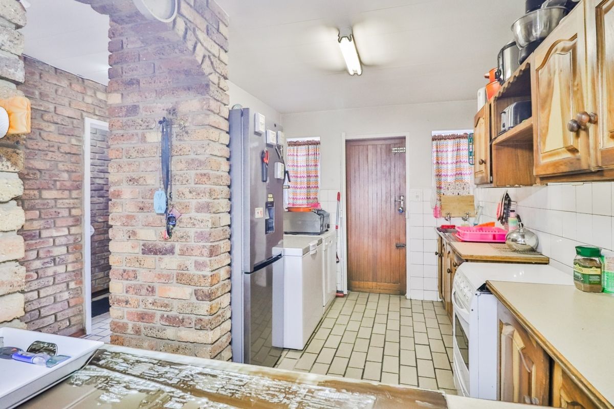 A dated kitchen featuring exposed brickwork, wooden cabinetry, tiled flooring, and a freestanding stove, offering potential for a modern renovation.