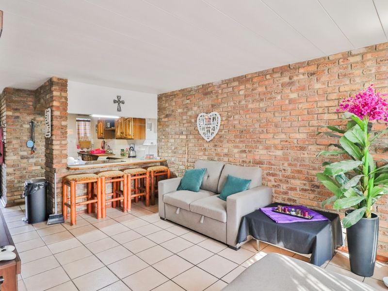 Open plan living area featuring an exposed brick feature wall, tiled flooring, and a breakfast bar connecting to the kitchen space.