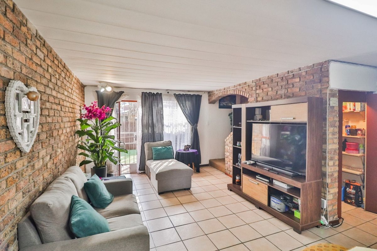 Living room featuring exposed brick walls, tiled flooring, and a distinctive brick archway leading to an adjacent space with access to the rear exterior.