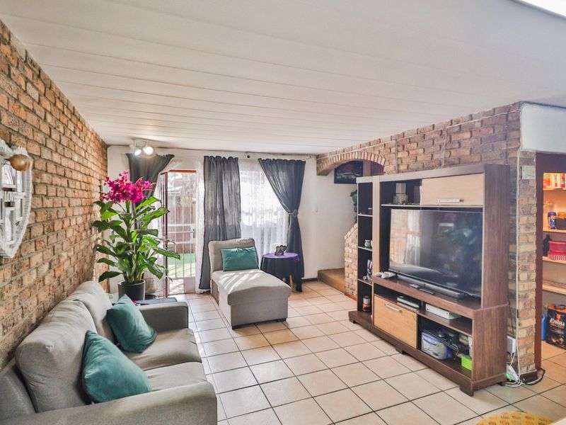 Living room featuring exposed brick walls, tiled flooring, and a distinctive brick archway leading to an adjacent space with access to the rear exterior.