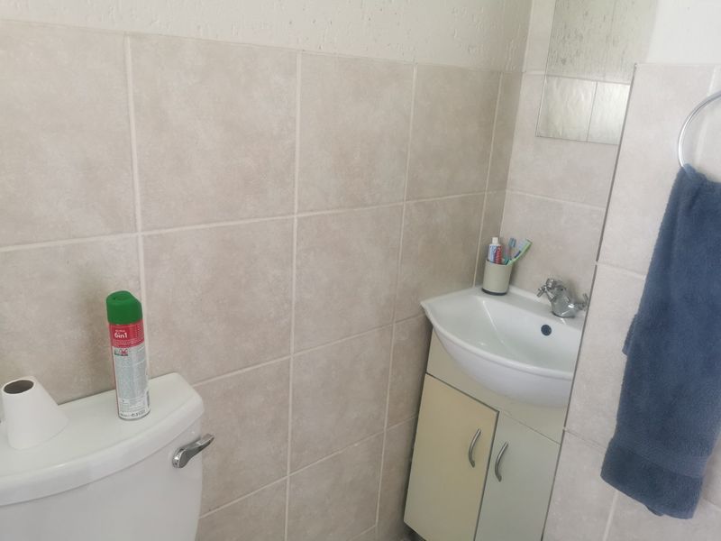 A functional bathroom featuring neutral ceramic wall tiles, a vanity cabinet with a washbasin, and a standard toilet.