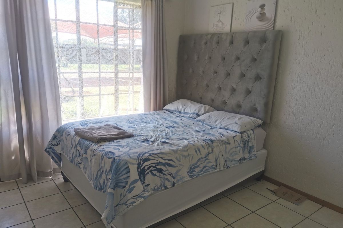 A bedroom featuring tiled flooring, textured walls, and a large window allowing natural light into the space.