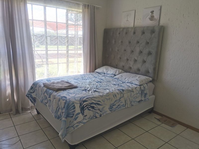 A bedroom featuring tiled flooring, textured walls, and a large window allowing natural light into the space.