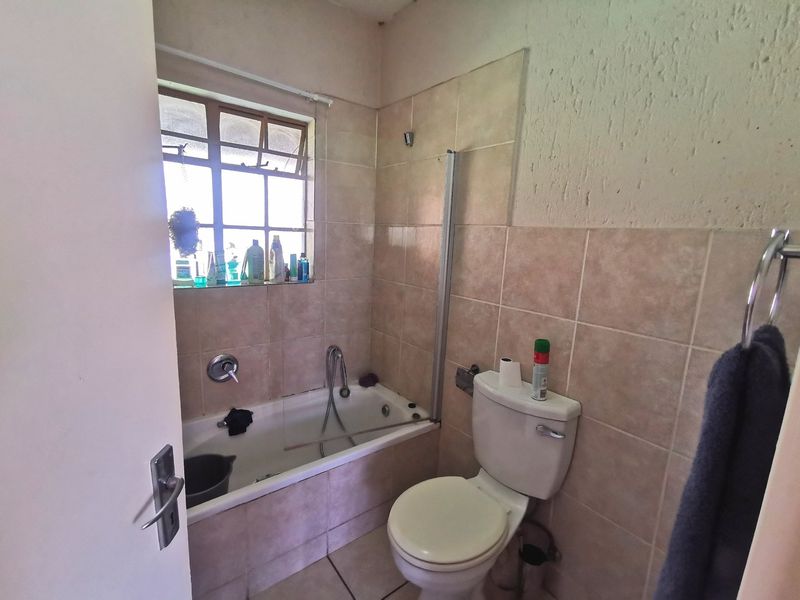 A compact bathroom featuring a bathtub with a shower screen, a standard toilet, and neutral wall and floor tiling.