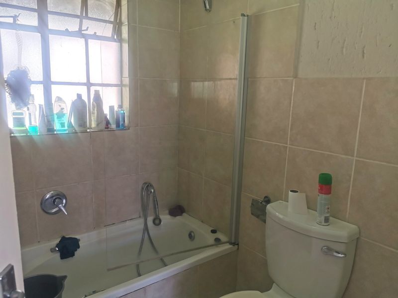 A functional bathroom featuring a bathtub with a shower mixer, glass screen, and a standard toilet, finished with neutral wall tiling.
