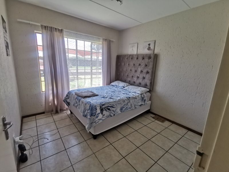 A functional bedroom featuring tiled flooring, textured walls, and a large window providing natural light.
