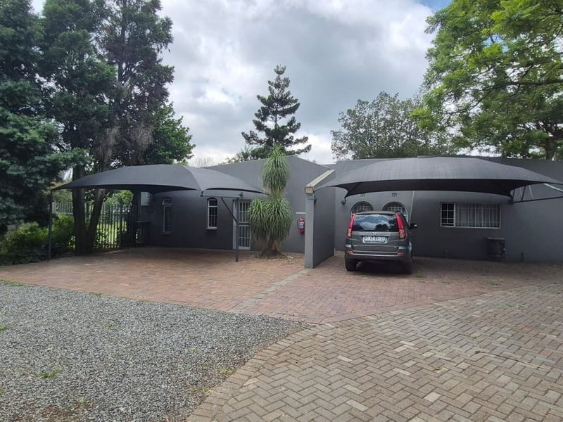 Front exterior view of the property featuring a paved driveway, gravel parking area, and two shade cloth carports for vehicle protection.