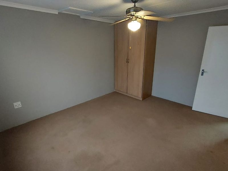A vacant bedroom featuring neutral grey walls, carpeted flooring, a built-in wardrobe, and a ceiling fan.