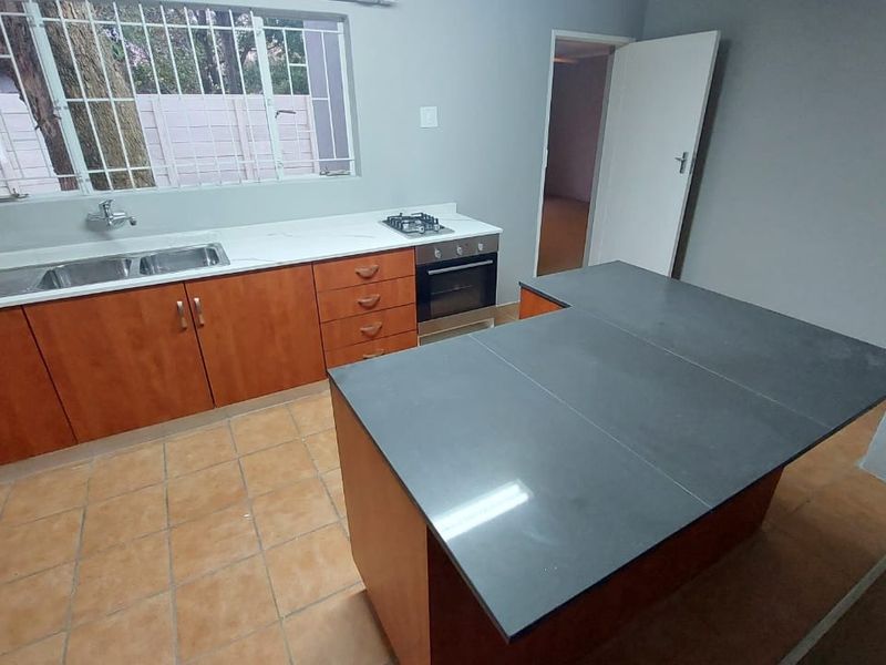 A functional kitchen featuring wooden cabinetry, a central island with a dark countertop, built-in oven, gas hob, and a double sink.