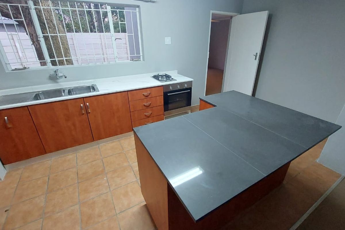 A functional kitchen featuring wooden cabinetry, a central island with a dark countertop, built-in oven, gas hob, and a double sink.