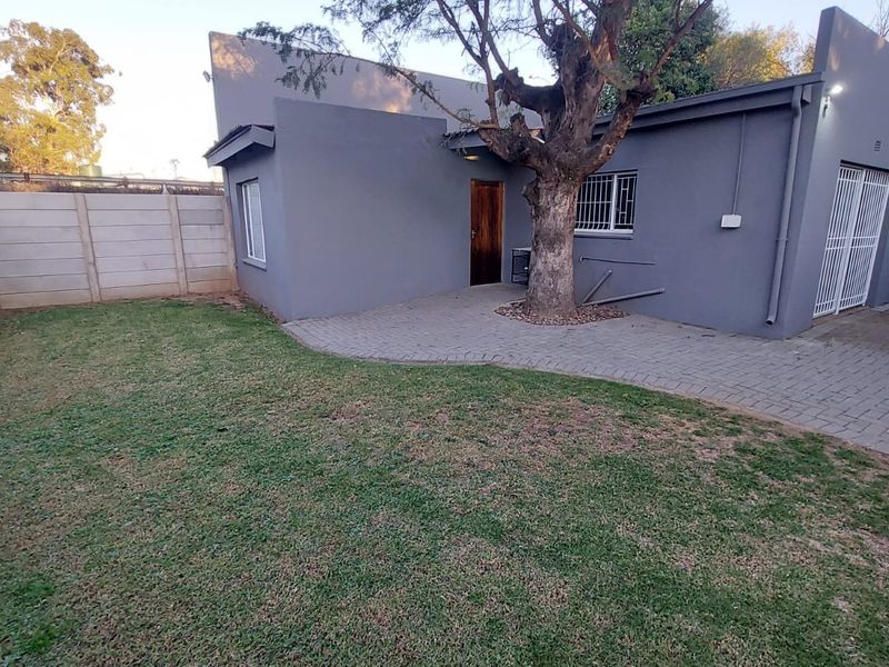 Rear exterior view of the property featuring a paved patio area, lawn, and secure boundary walling.