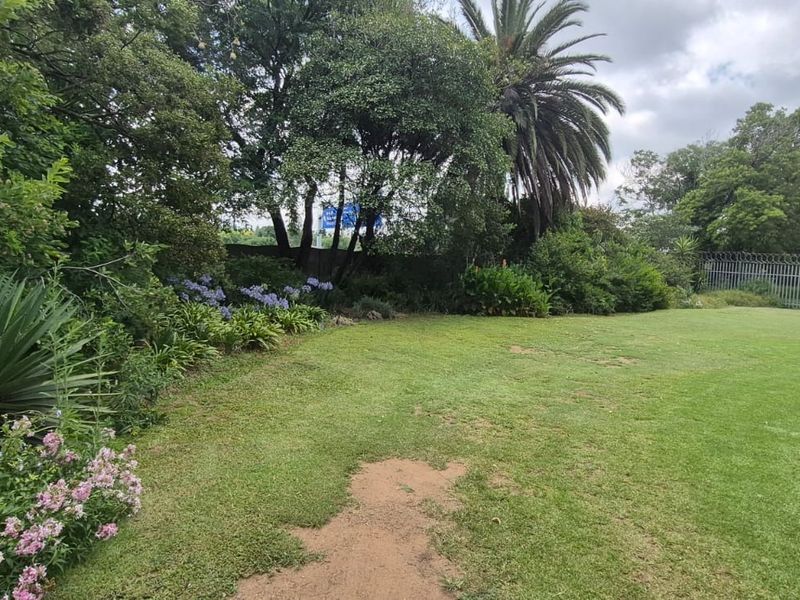 A spacious, established garden featuring a large lawn, mature trees, and perimeter security fencing.
