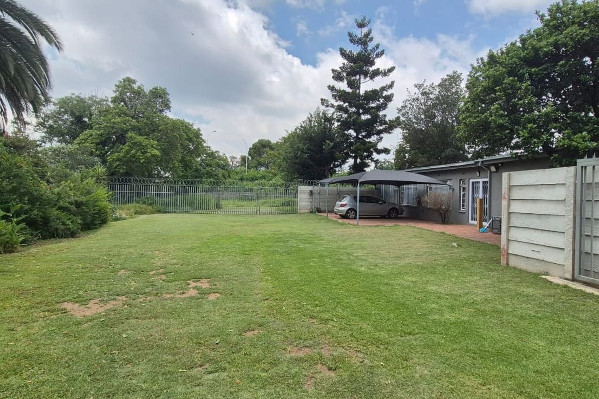 Spacious rear garden featuring a large lawn, a covered carport, and secure perimeter fencing with a sliding gate.