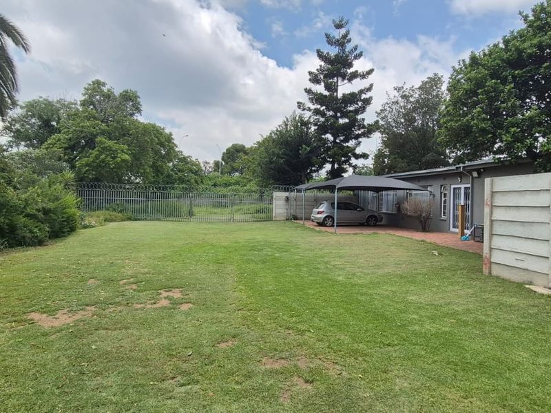 Spacious rear garden featuring a large lawn, a covered carport, and secure perimeter fencing with a sliding gate.